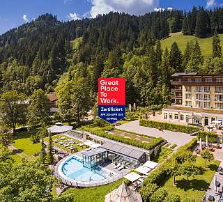 Hotelanlage mit Außenpool vor bewaldetem Berghang und sonniger Terrasse.